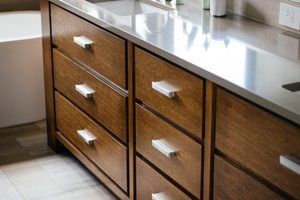 Wooden kitchen cabinets with silver handles beneath a gray countertop, viewed at an angle