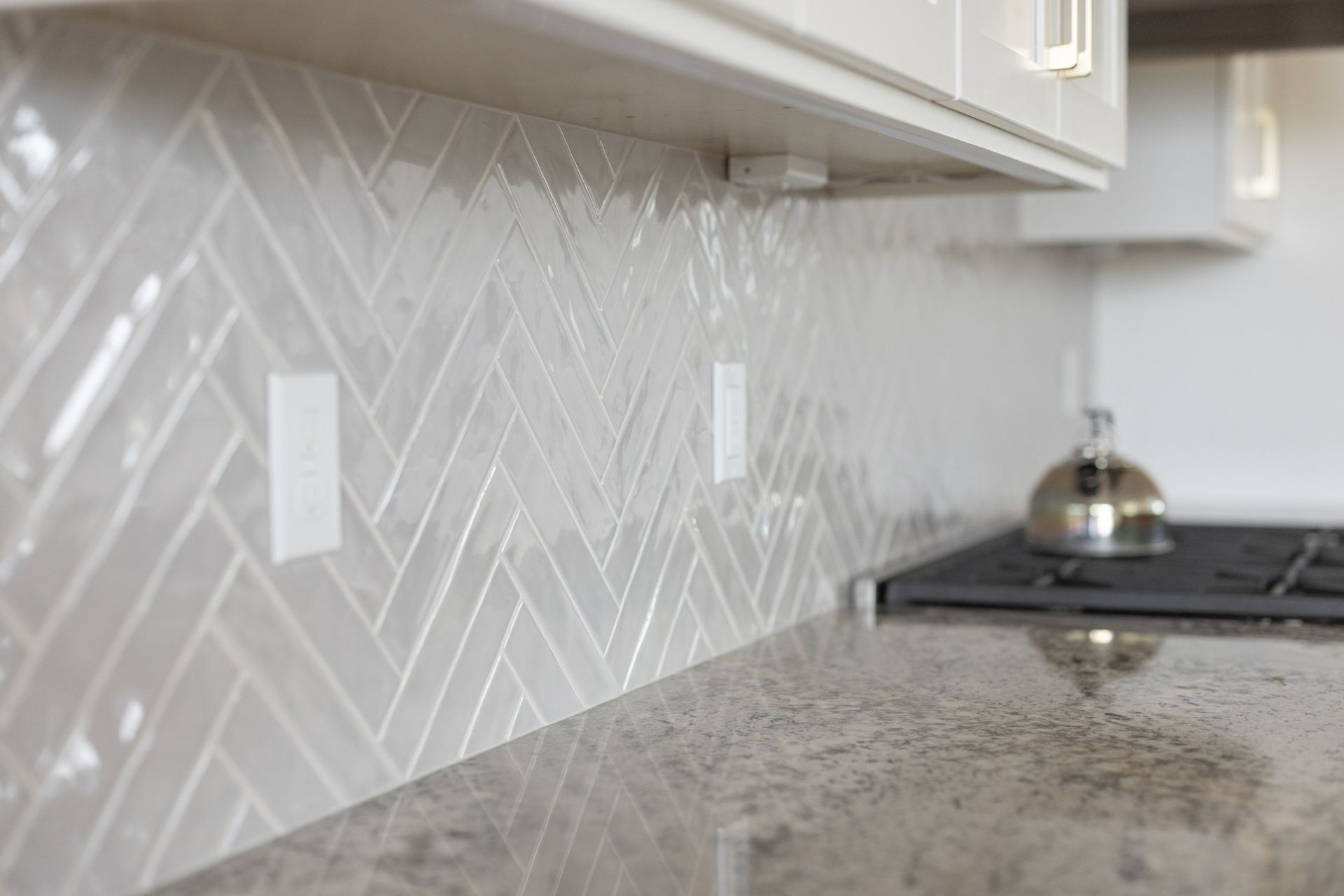 White chevron tile backsplash and granite kitchen countertop with a stovetop and kettle