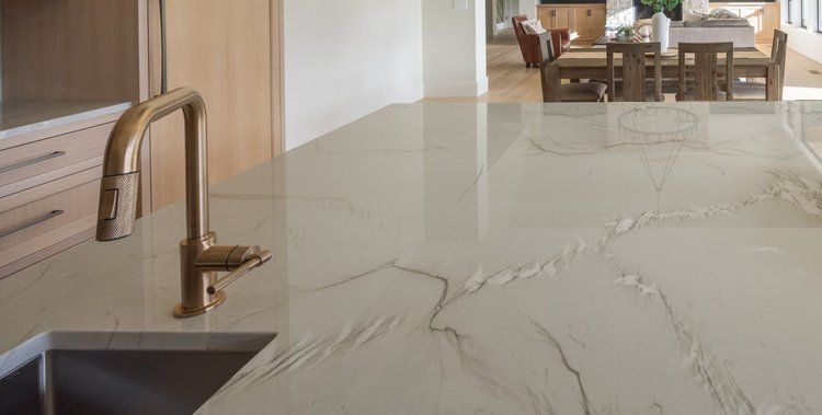 Modern kitchen with a marble island, brass faucet, and dining table in the background.