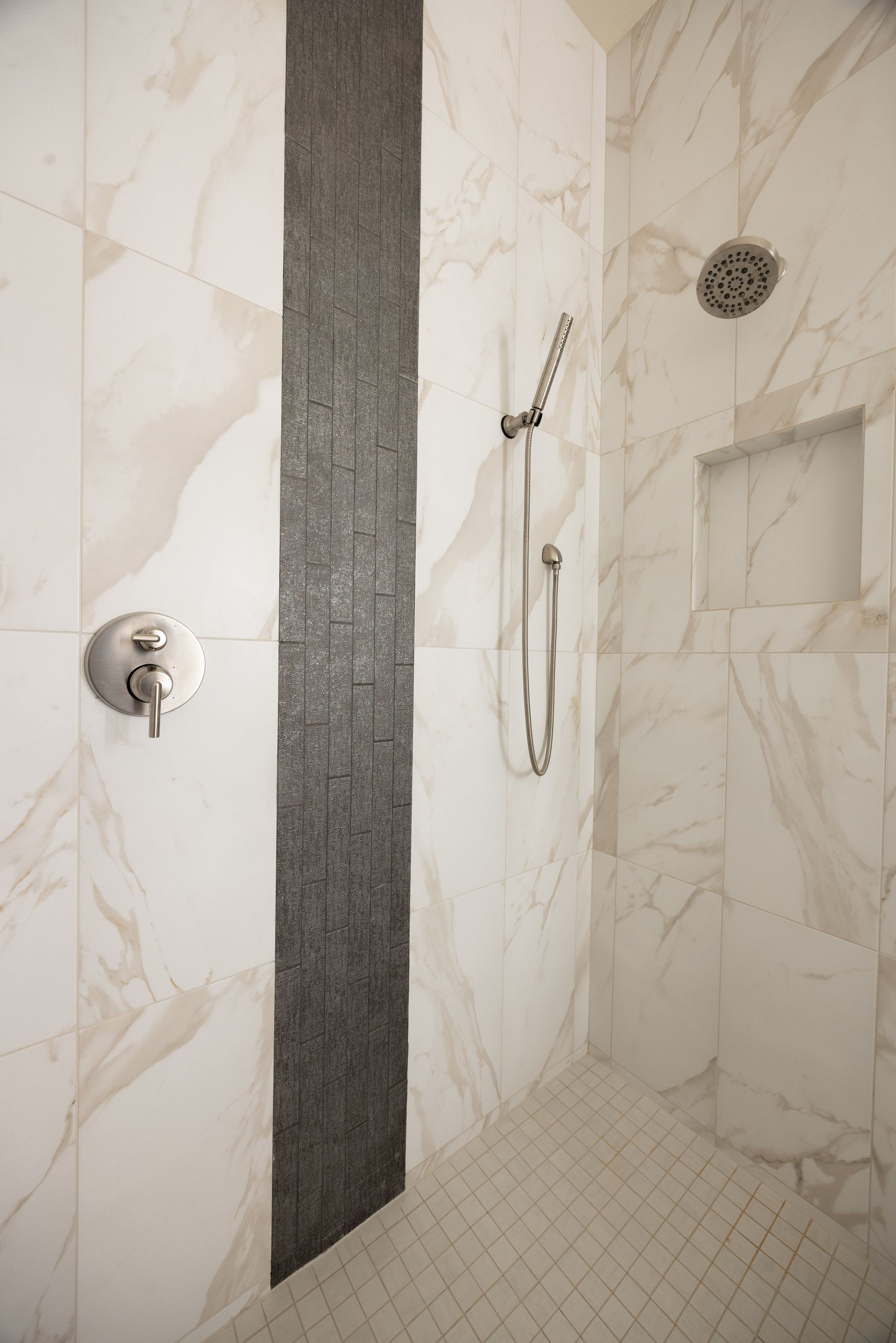 Modern shower stall with beige marble-look tile, dark vertical accent strip, and chrome shower fixtures