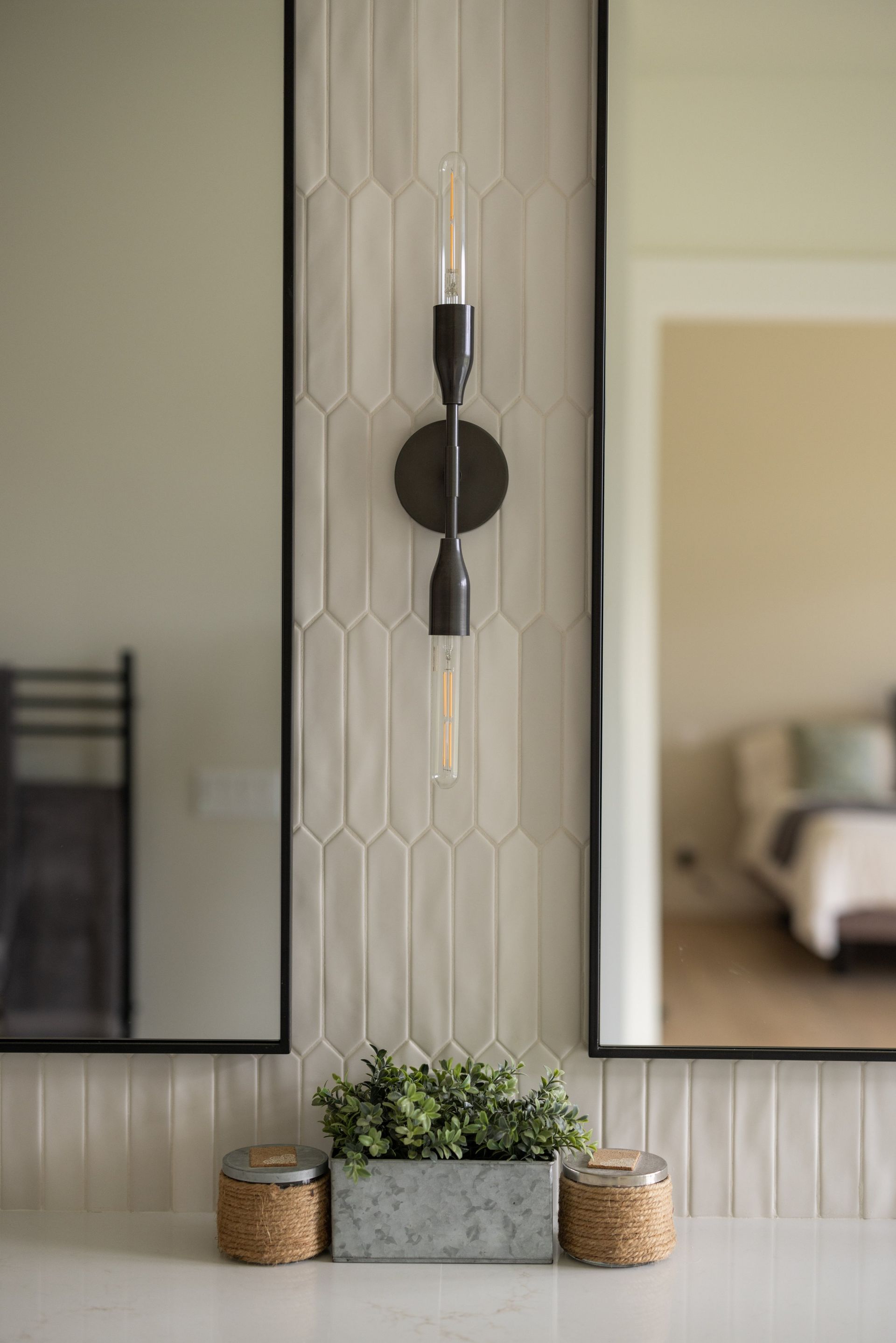 Modern wall sconces flanking a mirror above a console with plants and woven baskets
