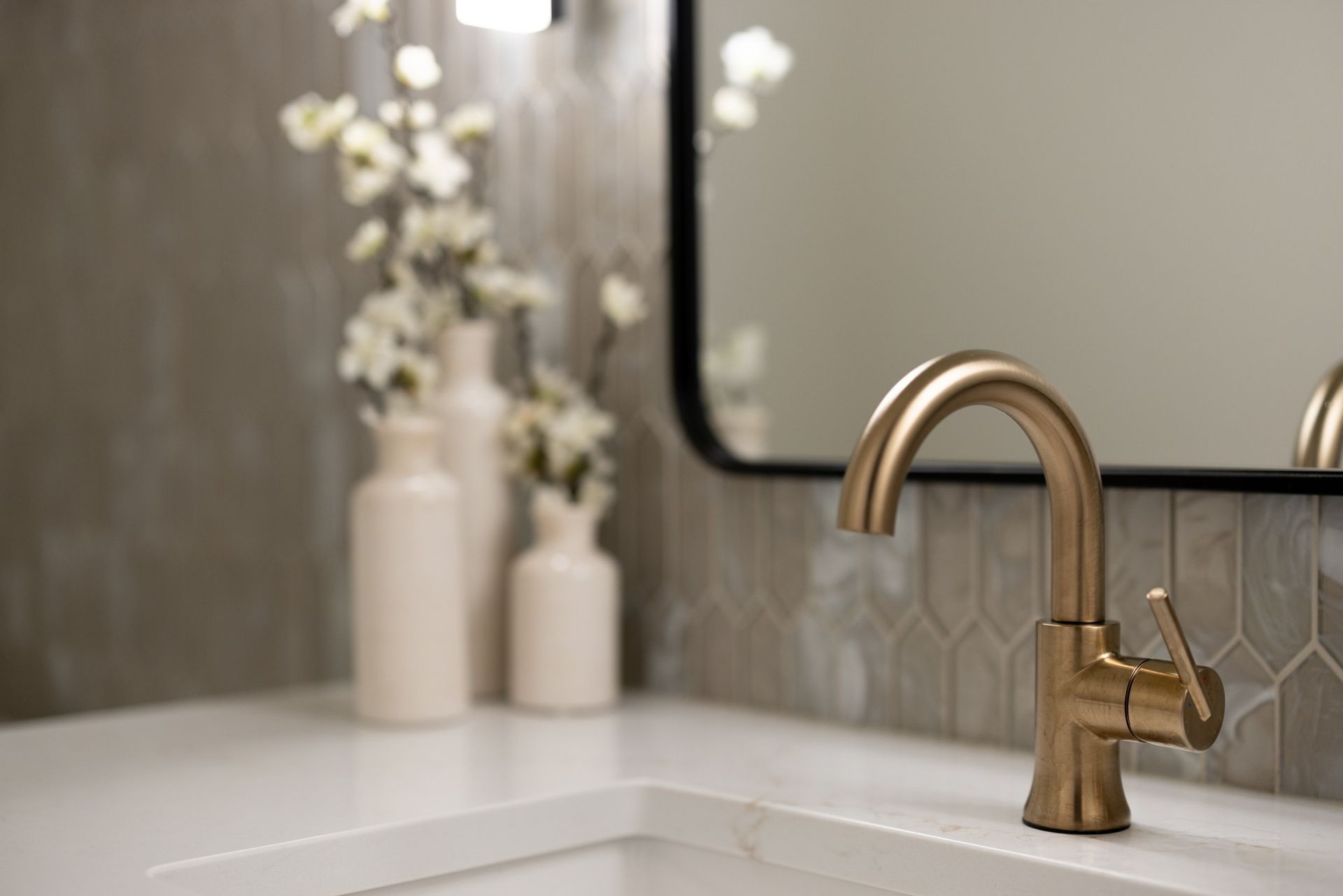 Modern bathroom vanity with brass faucet, white sink, and blurred flowers near a mirror