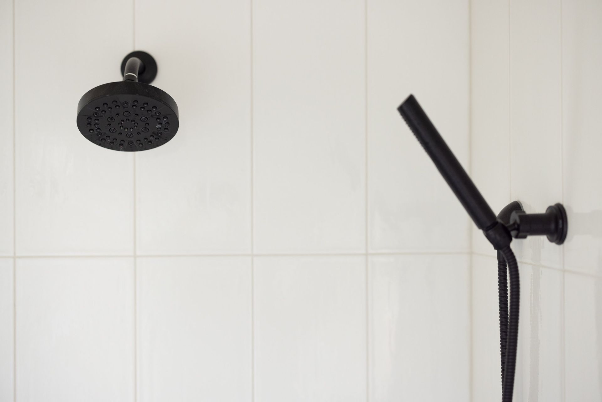 Black rain showerhead and handheld shower in a tiled bathroom