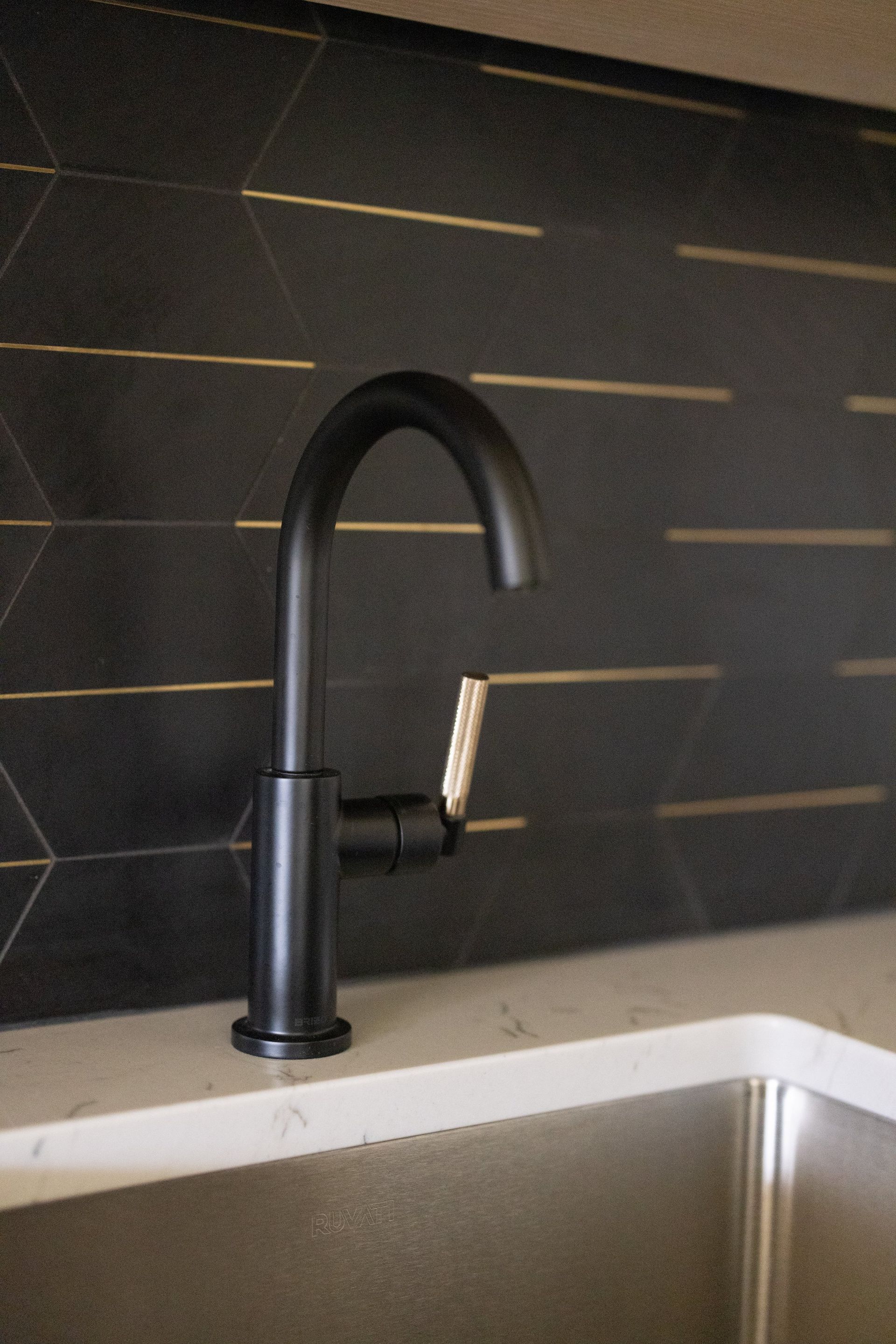 Black kitchen faucet over a sink against a dark tiled backsplash.