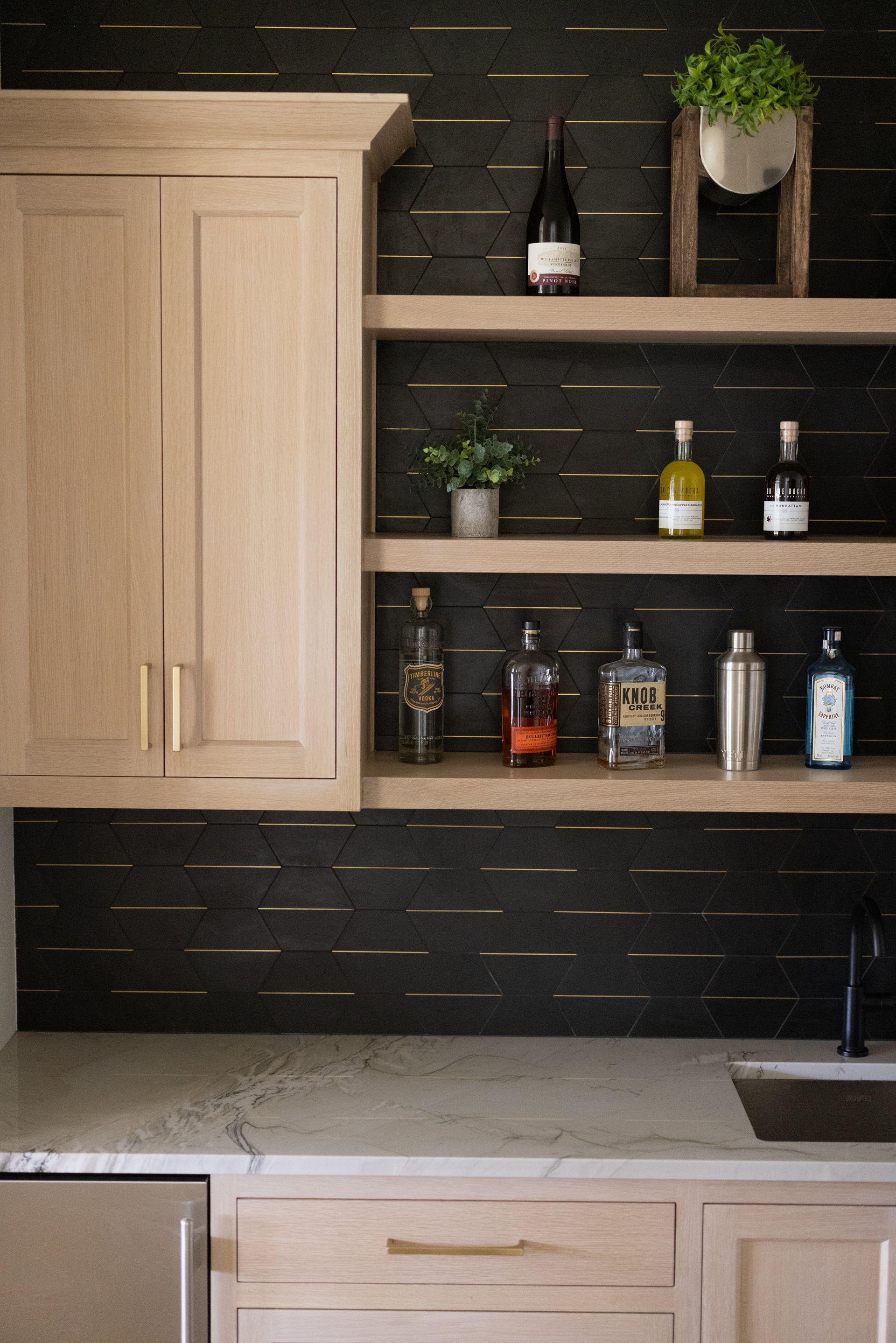 Modern kitchen with black tile backsplash, light wood cabinets, open shelves, and countertop decor.