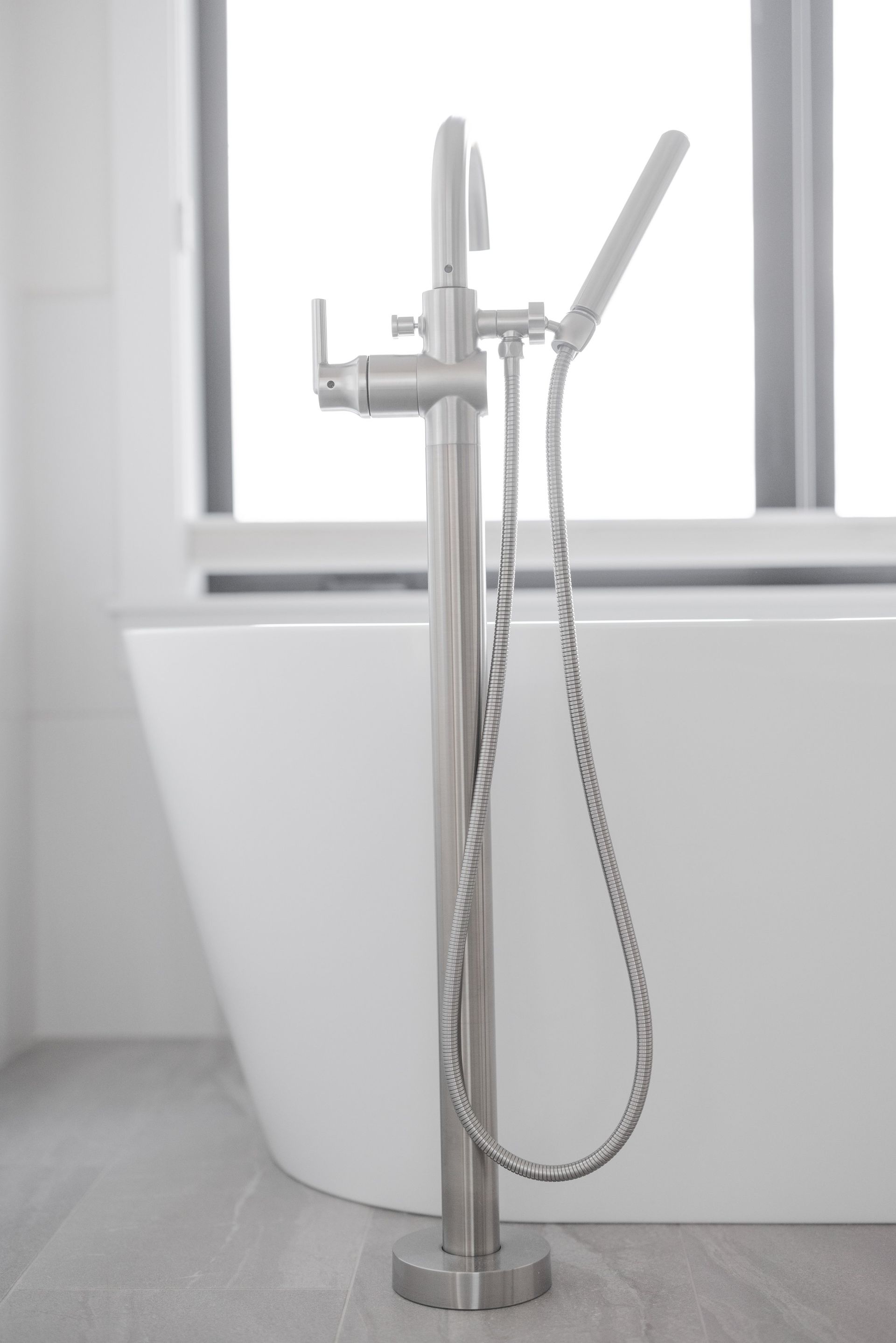 Chrome freestanding bathtub faucet with handheld sprayer in a bright bathroom