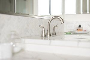 Bright bathroom sink with chrome faucet and white marble countertop near a window