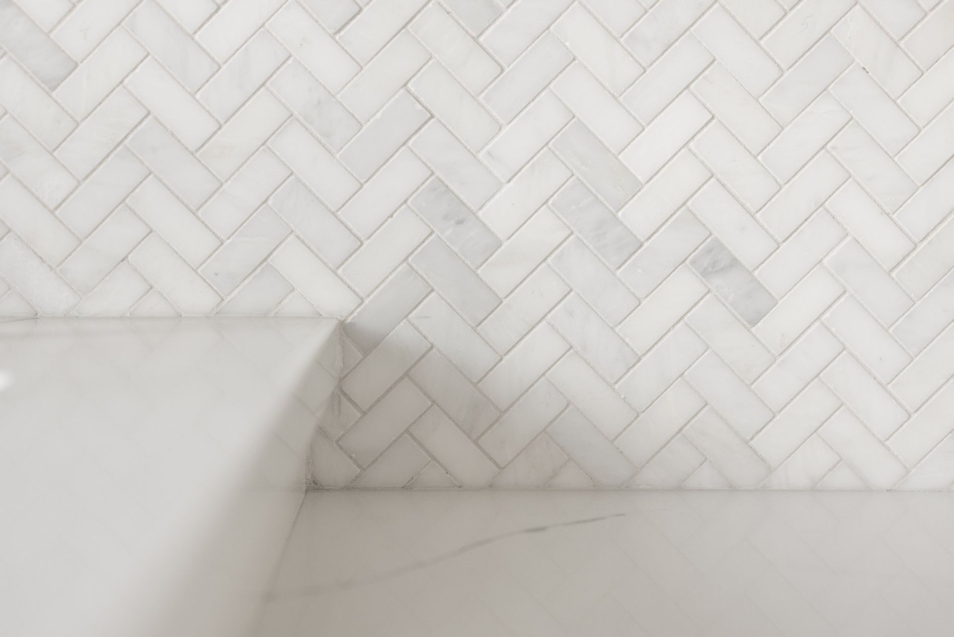 White herringbone tile backsplash above a light countertop or sink edge