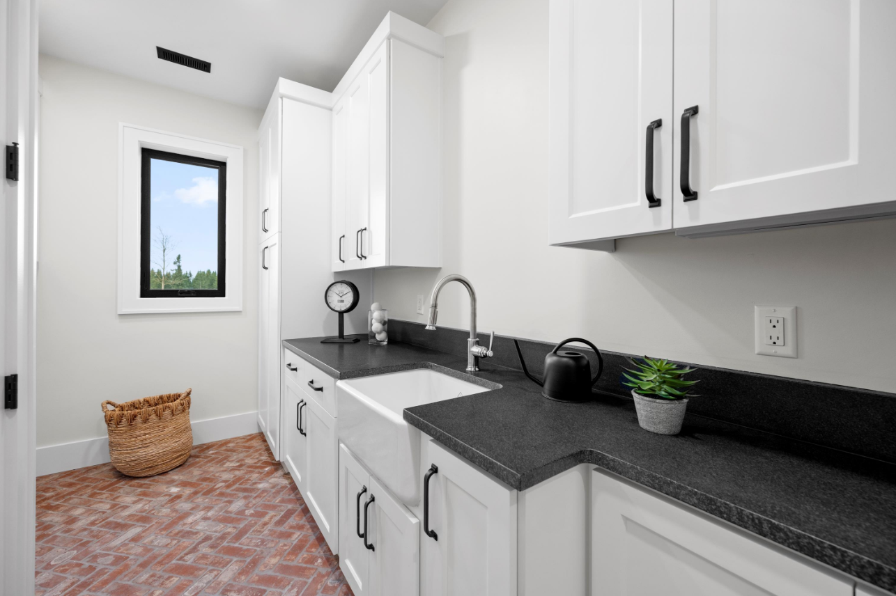 Bright white kitchen with black countertops, sink, cabinets, and a window over a patterned rug.
