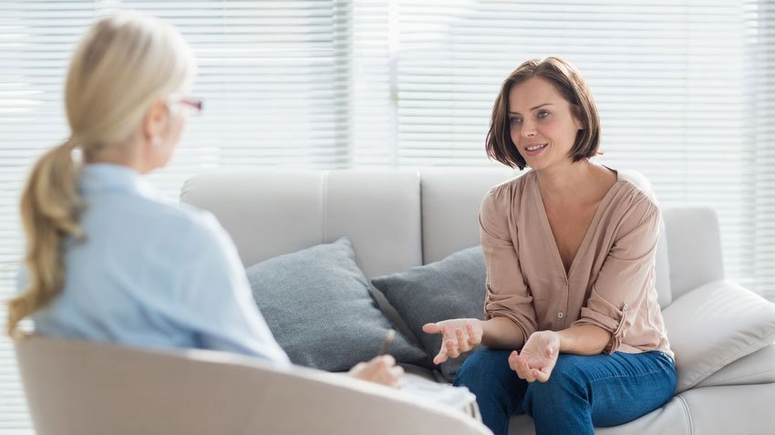 Two women are sitting on a couch talking to each other.
