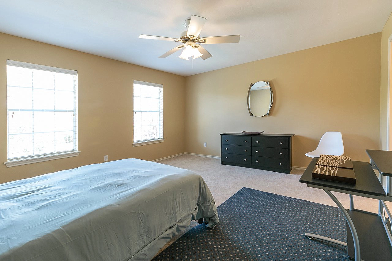 A bedroom with a bed , dresser , desk and ceiling fan.