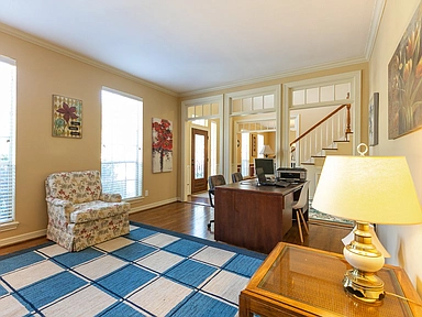 A living room with a desk , chair , lamp and rug.