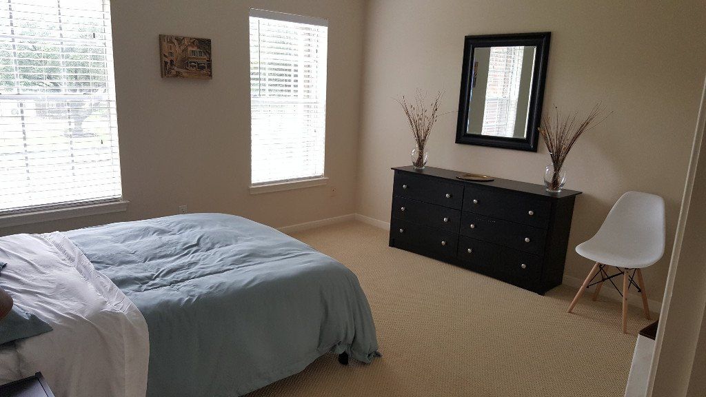 A bedroom with a bed , dresser , chair and mirror.