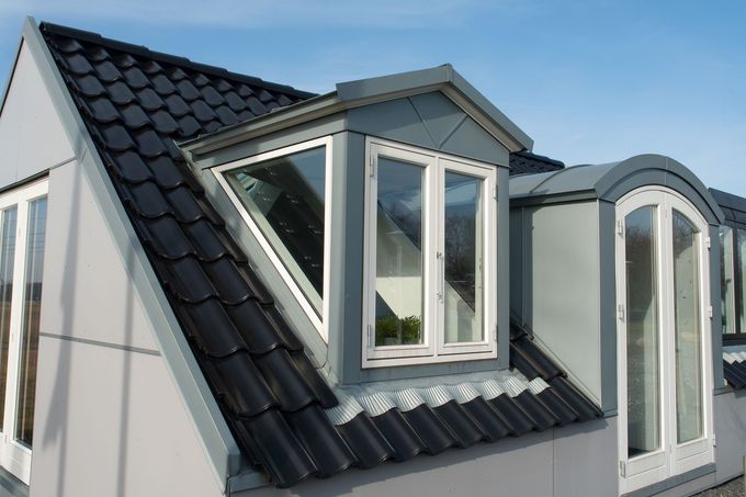 Modern house dormer with black roof and white-framed windows under a blue sky