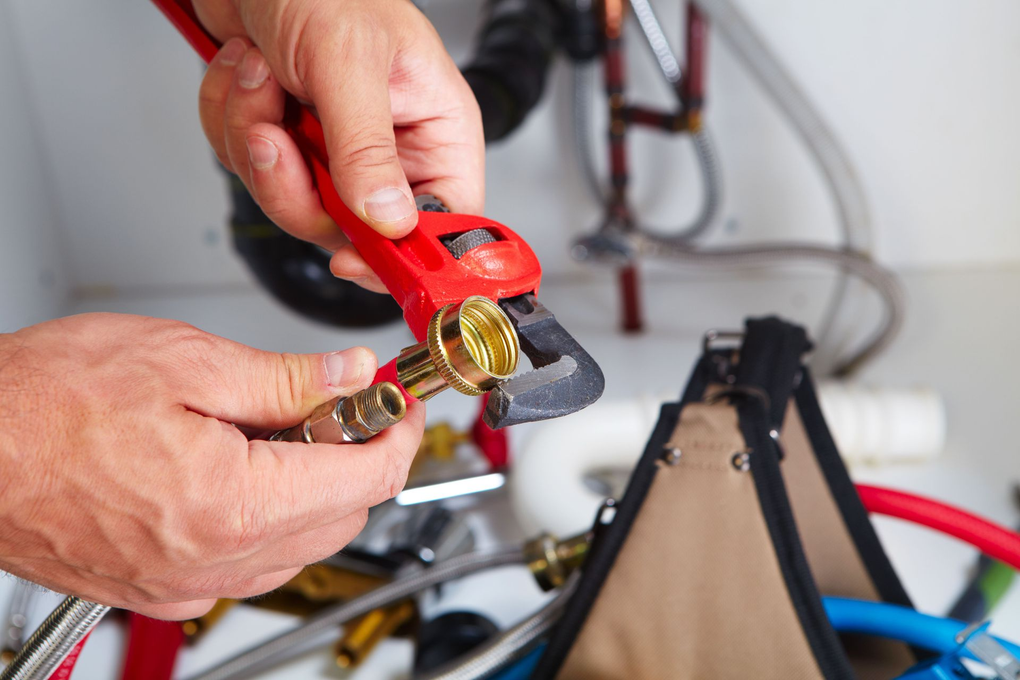 Hands using a red wrench to adjust a brass fitting on a bicycle frame.