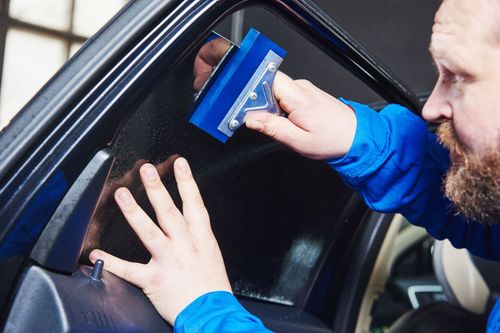 Person using a blue squeegee to clean a car window from inside the vehicle