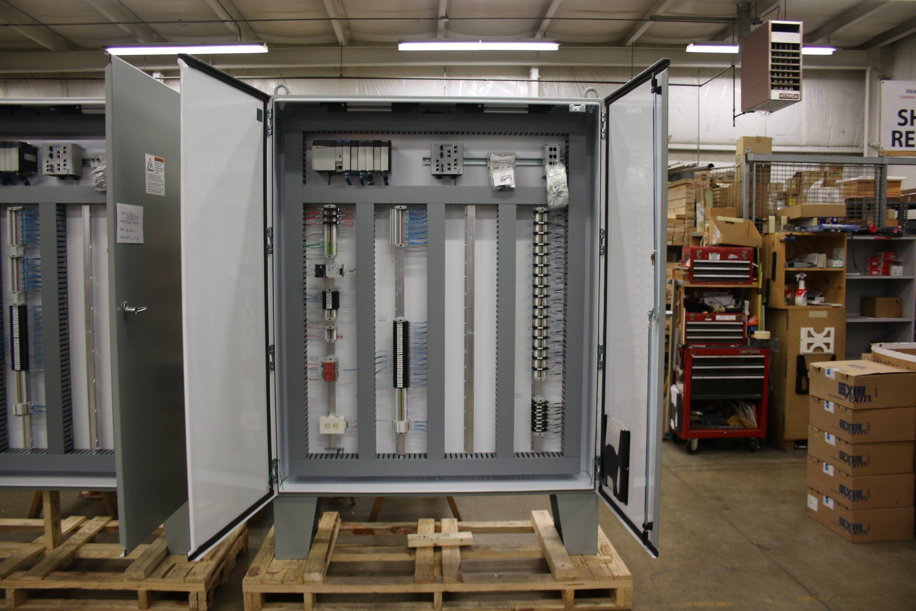 Three electrical cabinets are sitting on wooden pallets in a warehouse.