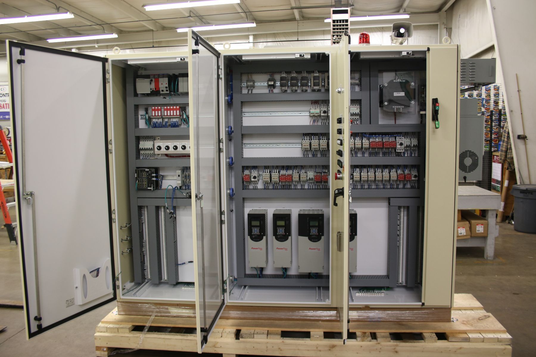 A large electrical control panel is sitting on a wooden pallet in a factory.