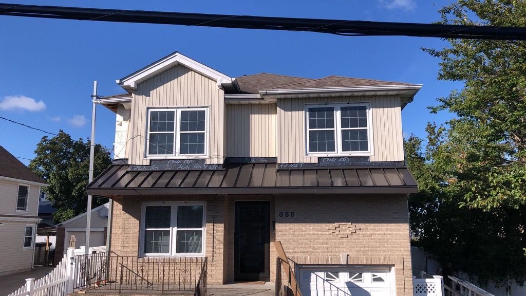 A two-story house with a tan brick lower level, beige siding on the upper level, and a dark metal awning over the entrance.