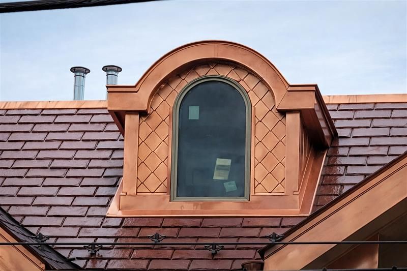 A copper-clad arched dormer window set into a dark, shingled roof.