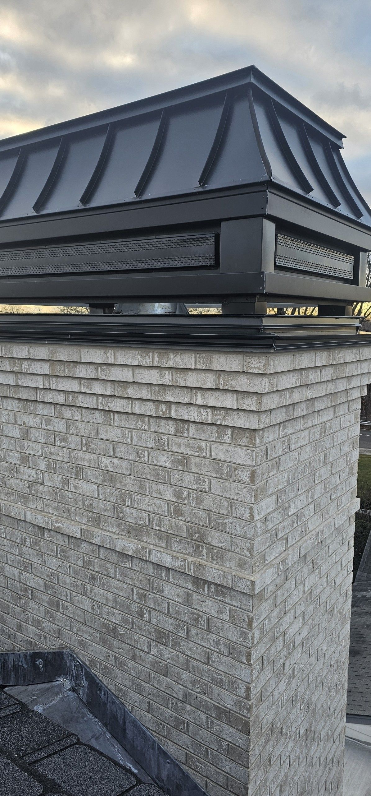 Close-up of a chimney with a black metal cap. The chimney is made of textured gray stone.