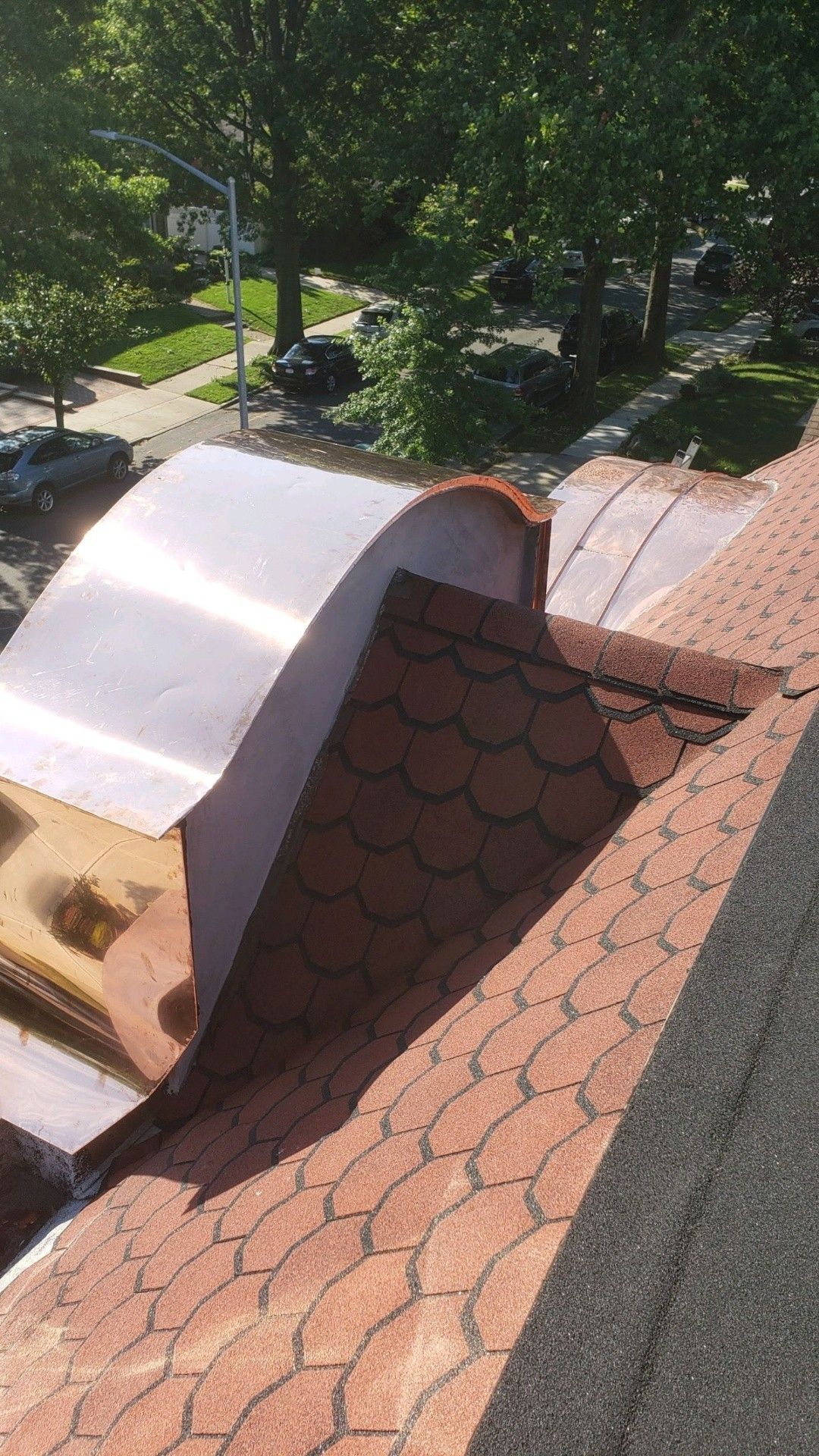 Copper flashing on a roof with orange shingle. Green trees and street in background.
