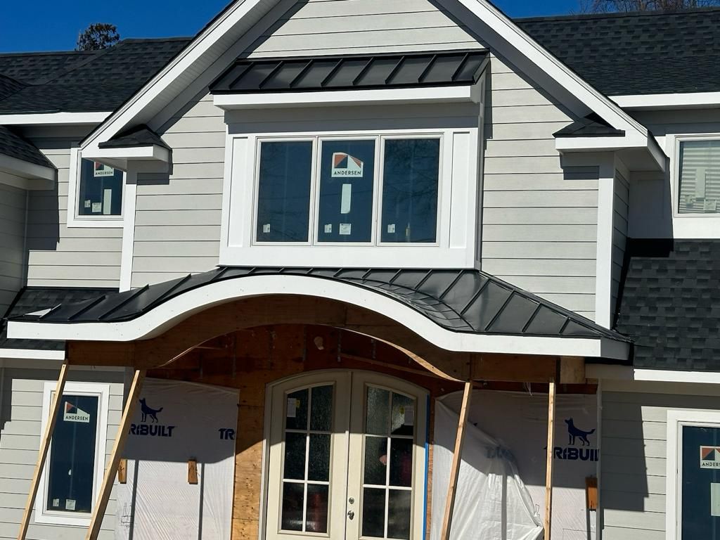 New construction house with gray siding, black roof, white trim, and a curved portico.