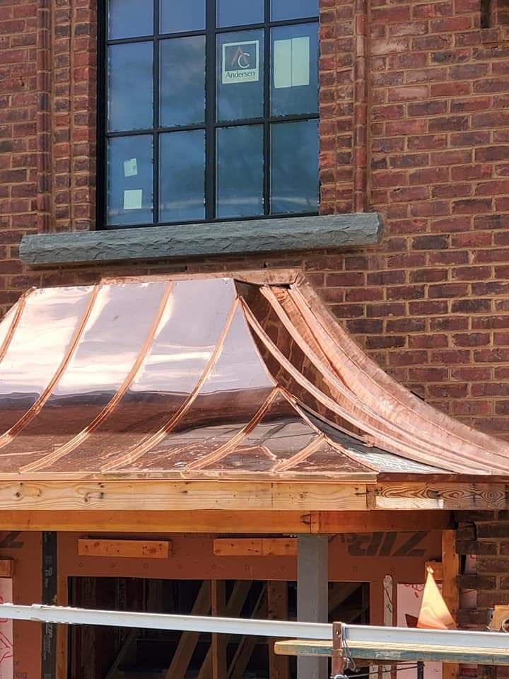 Copper roof over a doorway, attached to a brick building with a black window.