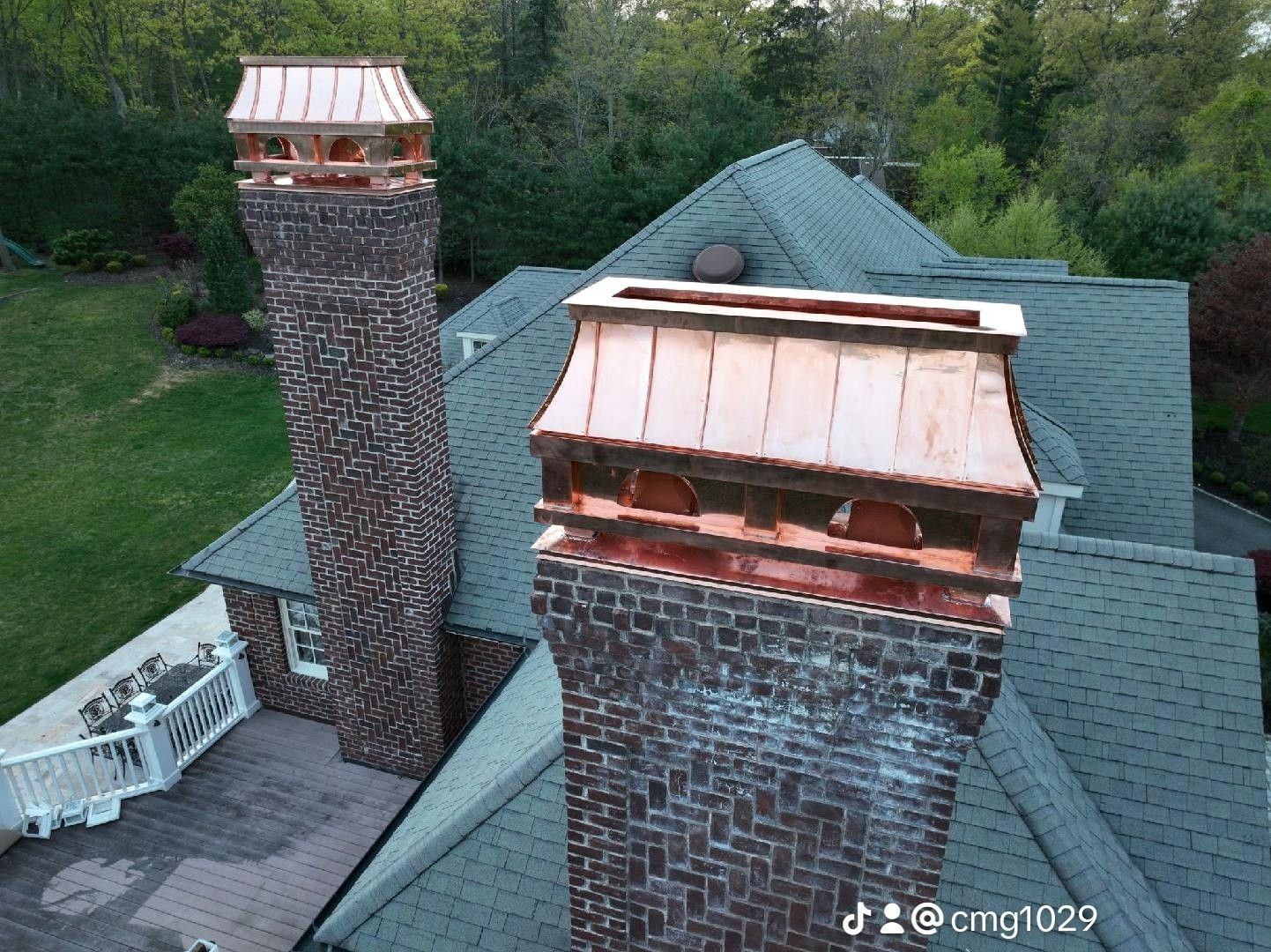 Two brick chimneys with copper caps on a house, viewed from above, surrounded by trees.