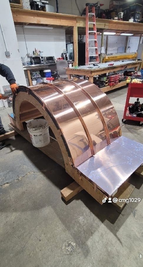 Copper roofing being installed on an arched structure in a workshop.