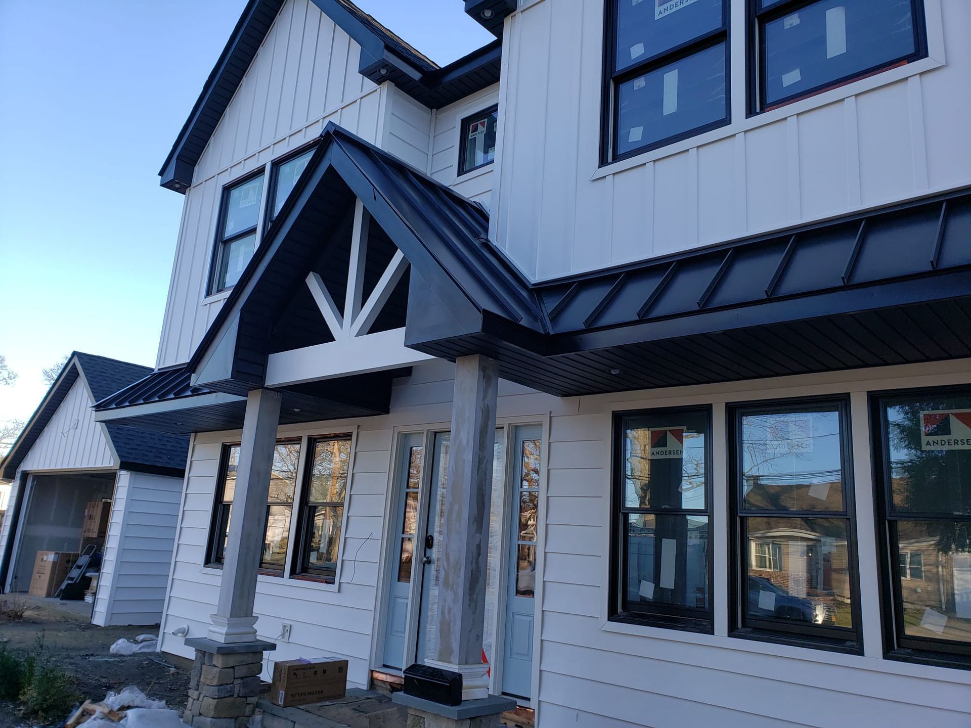 Two-story white house with black trim, windows, and roof; front porch; clear blue sky.