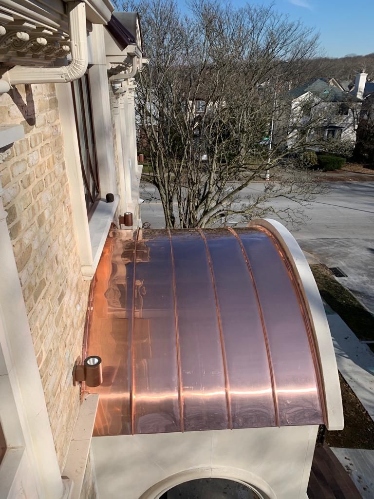 Copper roof on building with a curved design, visible from above, with surrounding trees and street.