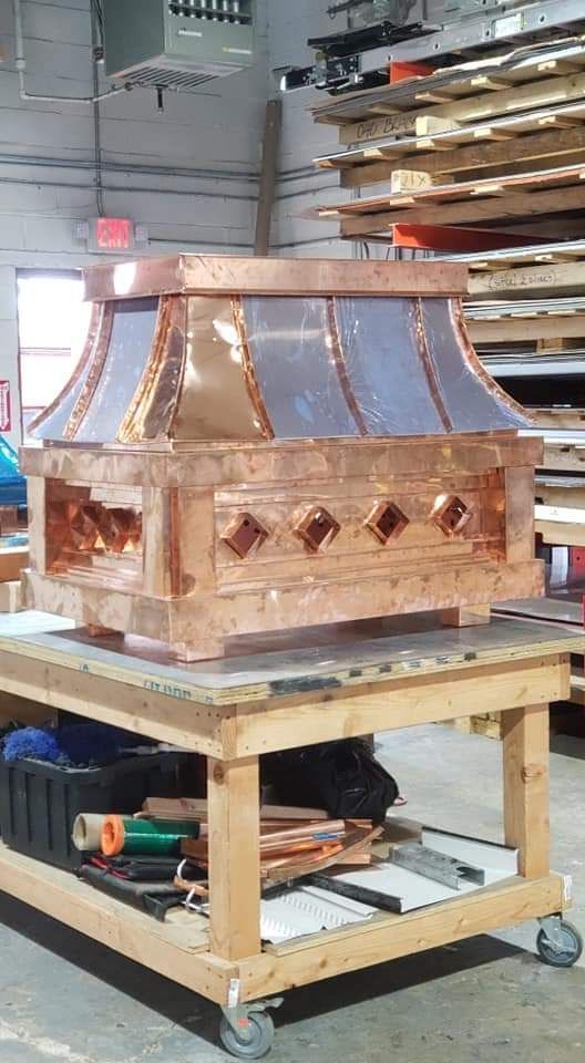 Copper range hood on a wooden workbench in a workshop.