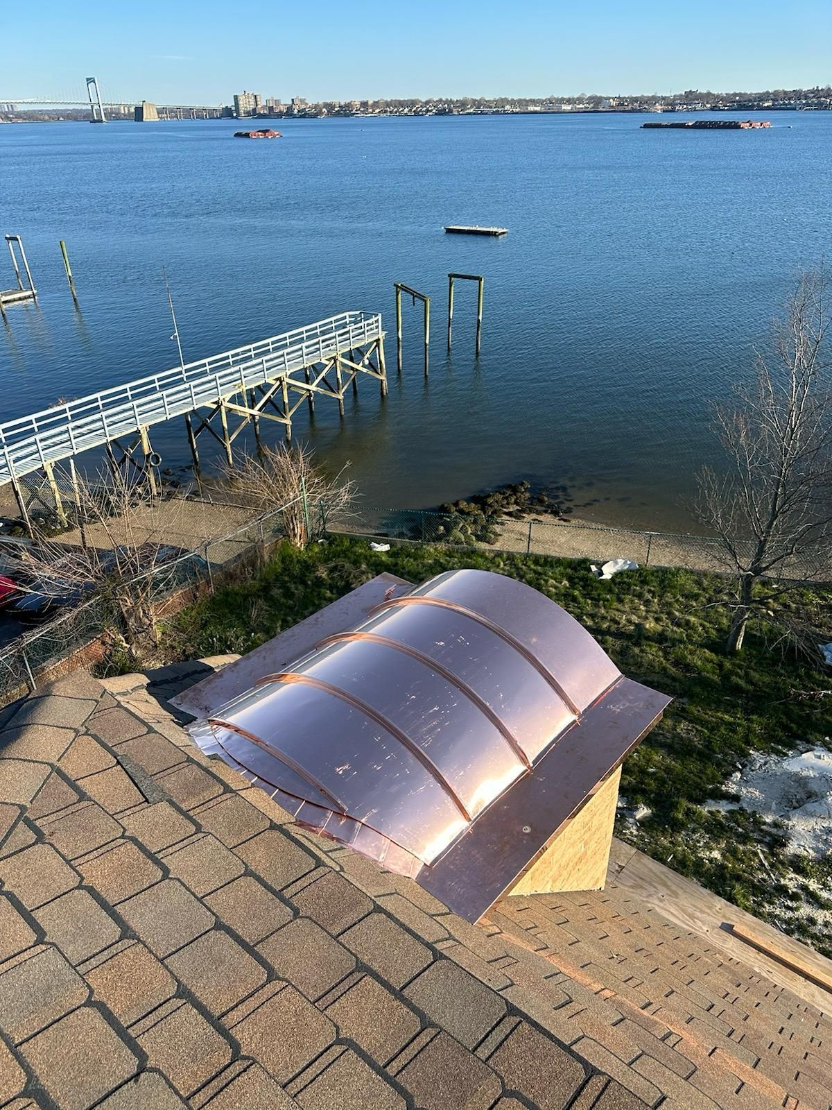 Copper chimney cap on a shingled roof overlooking water and a pier under a blue sky.