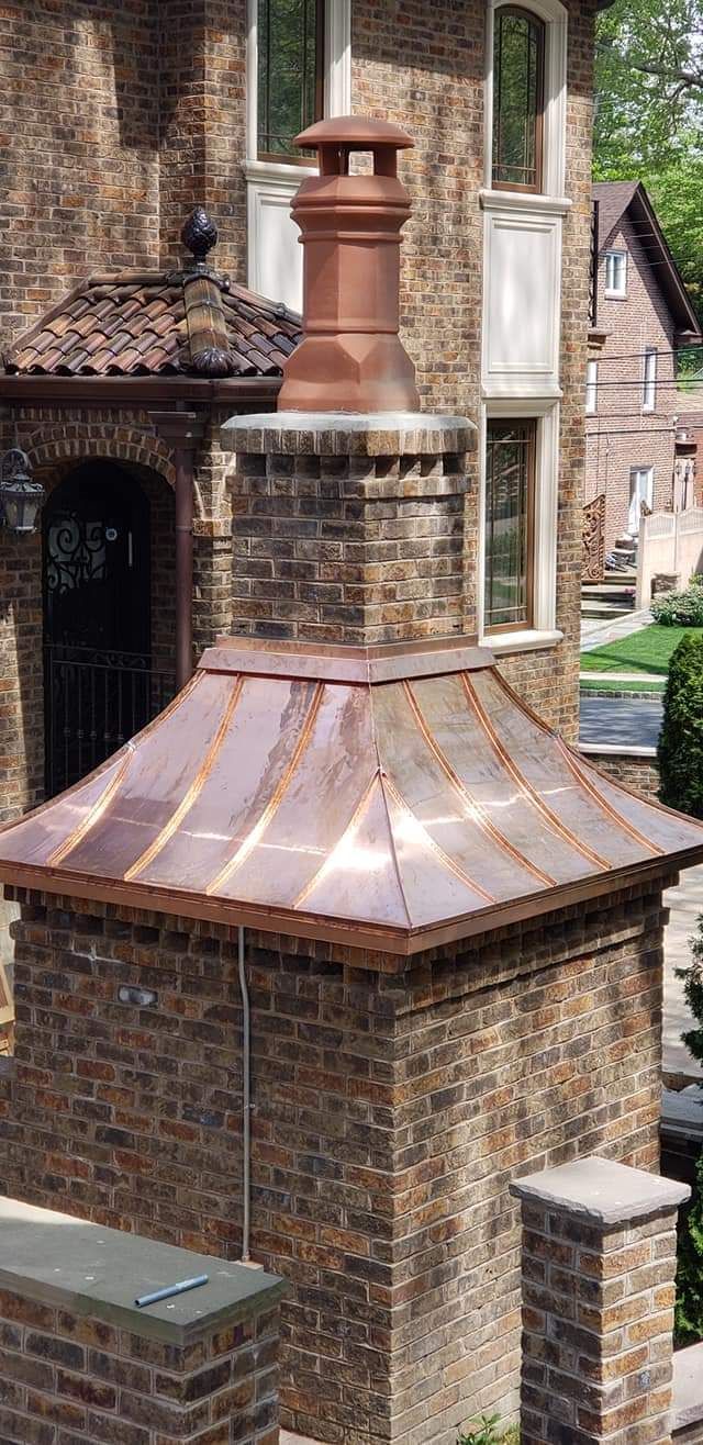 Brick chimney with a copper roof and cap on a brick building.