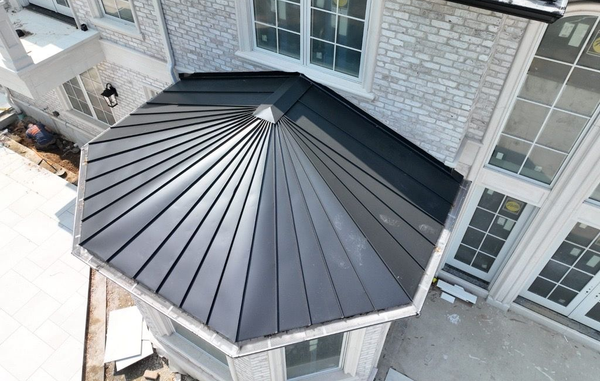 High-angle view of a modern, multi-faceted dark metal roof on a building with stone siding and large glass windows.