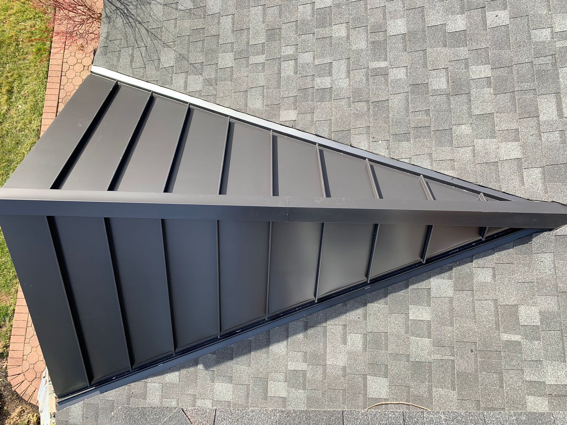 A dark gray standing seam metal roof section installed over an existing shingled roof.