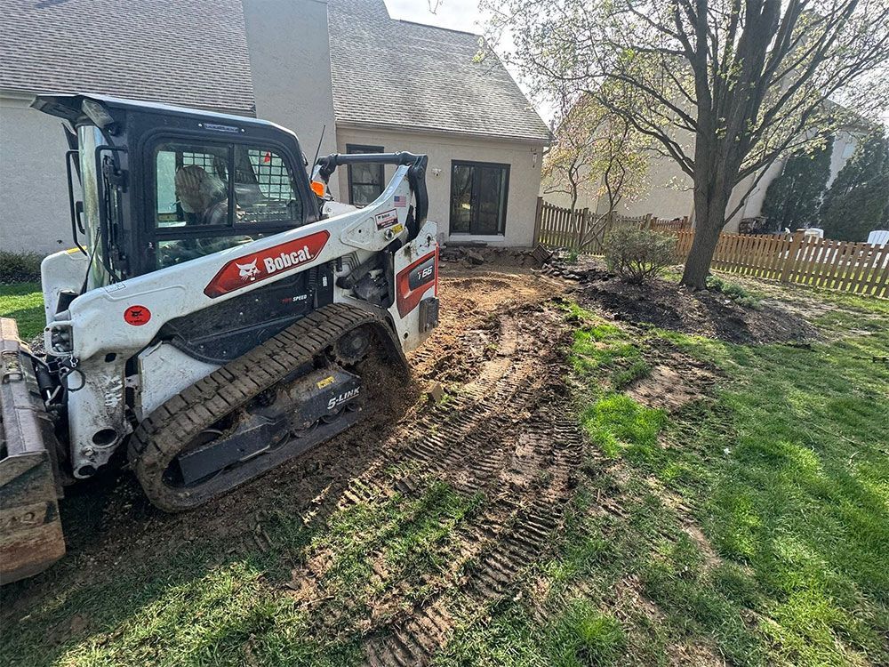 Compact track loader grading soil beside a house and tree in a yard