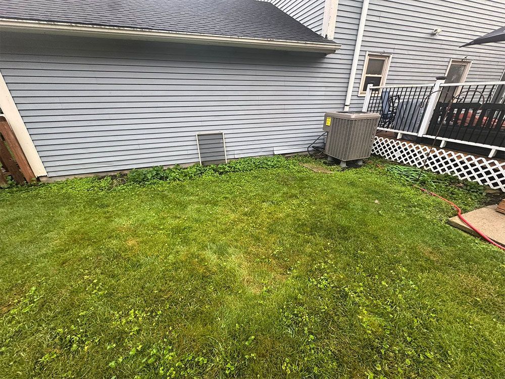 Backyard lawn beside gray house siding, with an air conditioner and fence corner.
