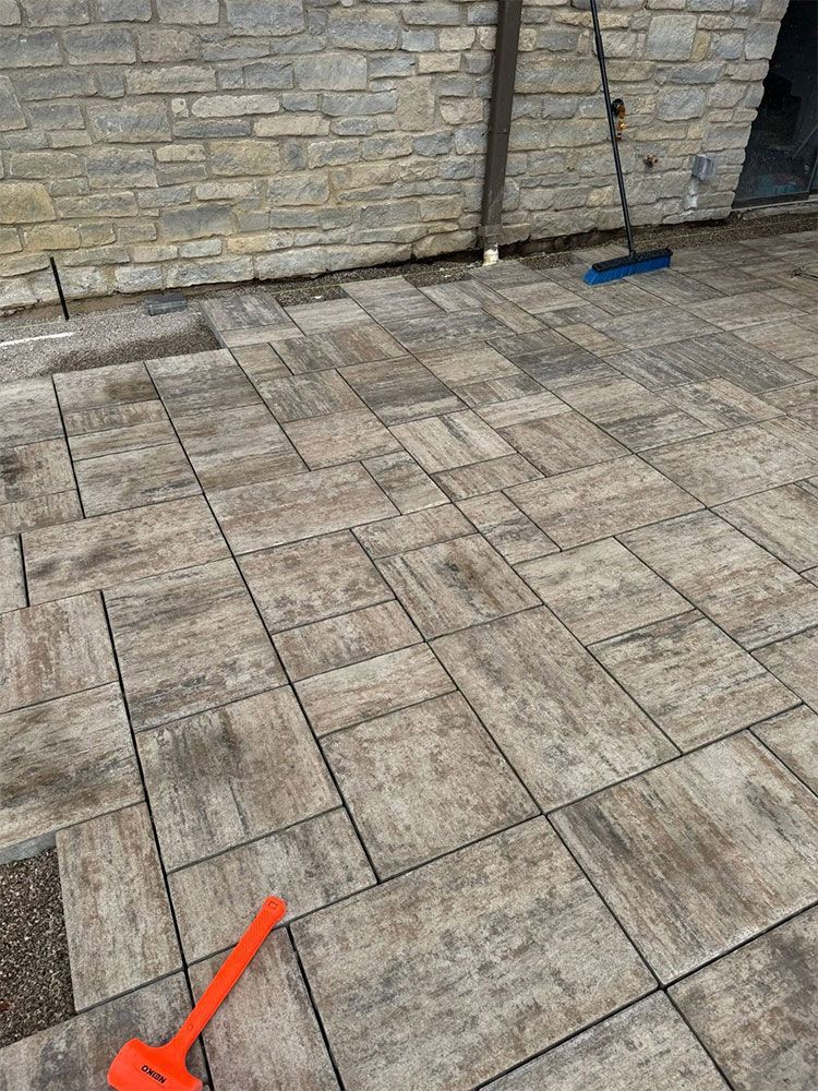 Stone patio with a stone wall, a broom, and a red arrow marking a spot on the ground
