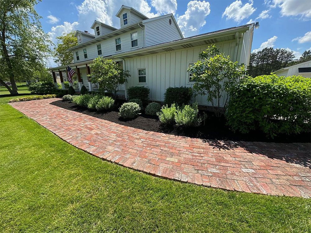 White house with brick walkway, green lawn, and trimmed bushes on a sunny day