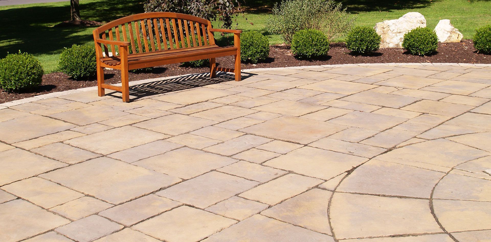 Wooden bench on a stone patio in a sunny garden with shrubs and a winding path