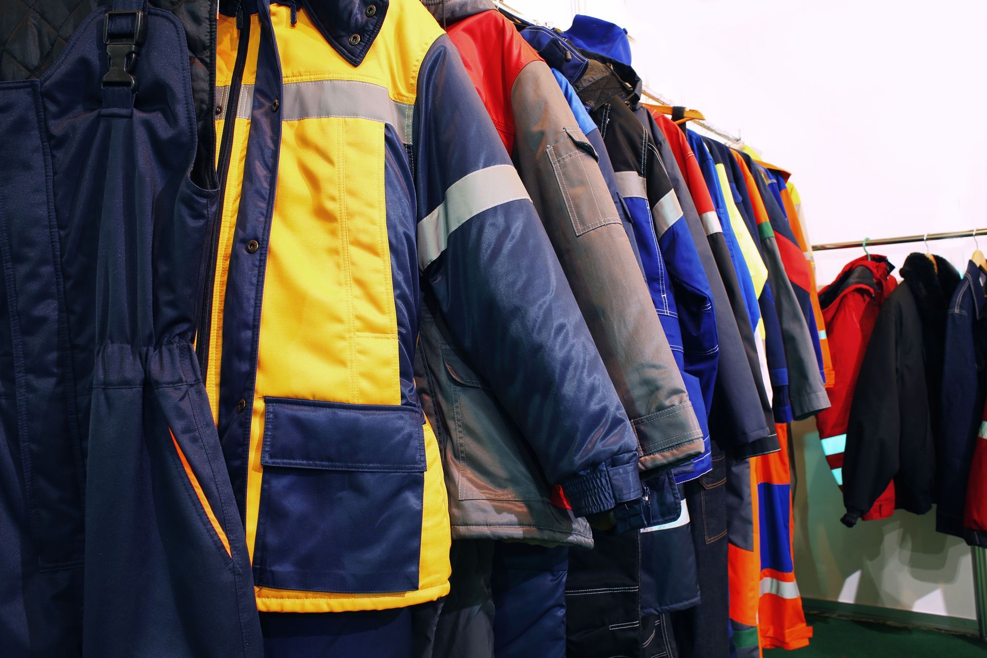 Winter work clothes hanging on a rack, in blue, yellow, and orange with reflective stripes.
