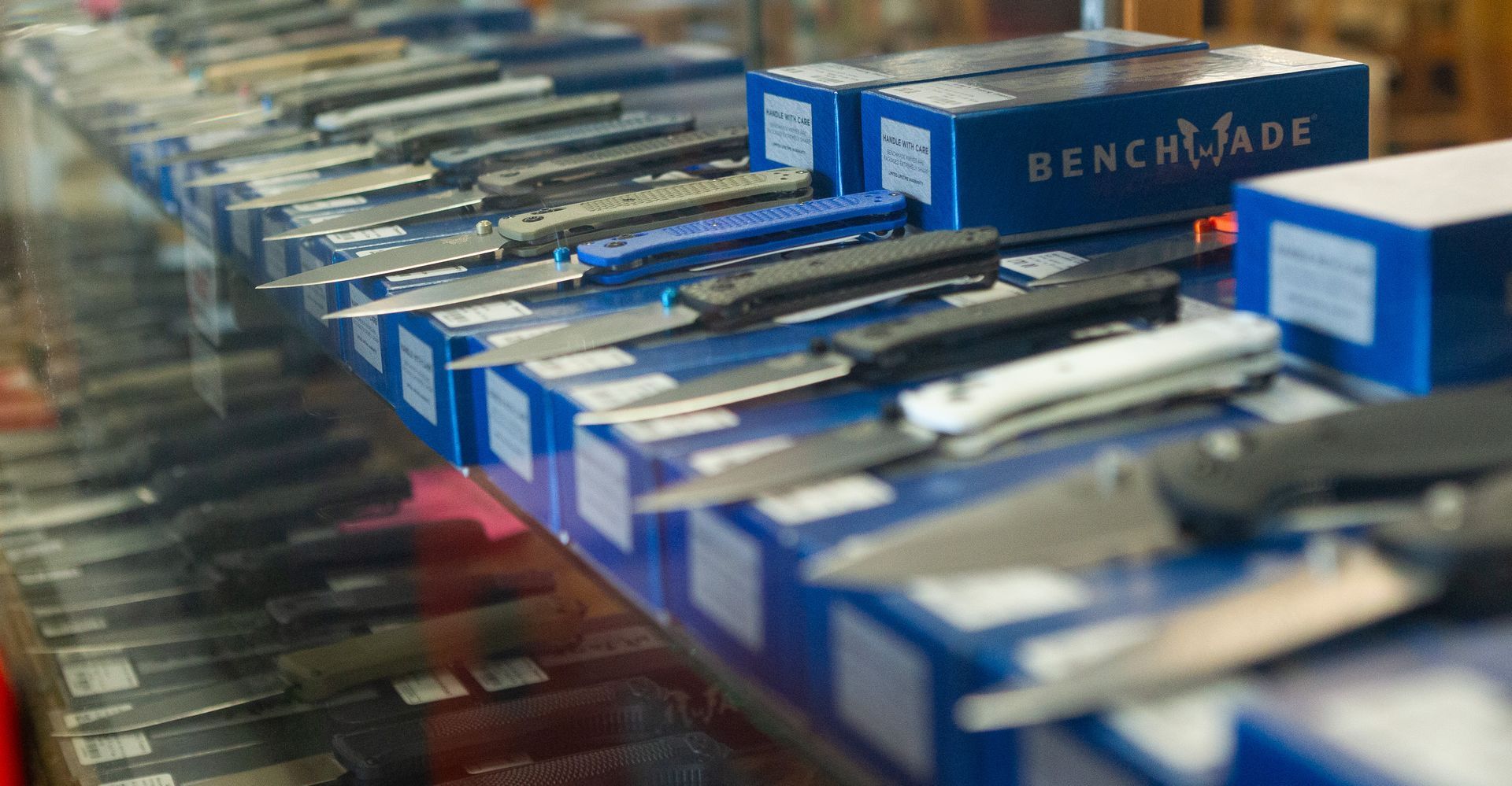 Display case filled with open pocket knives, many with blue Benchmade boxes.