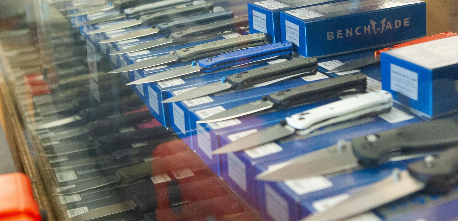 Knives on display inside a glass case, with some resting on blue boxes. A red label is visible.