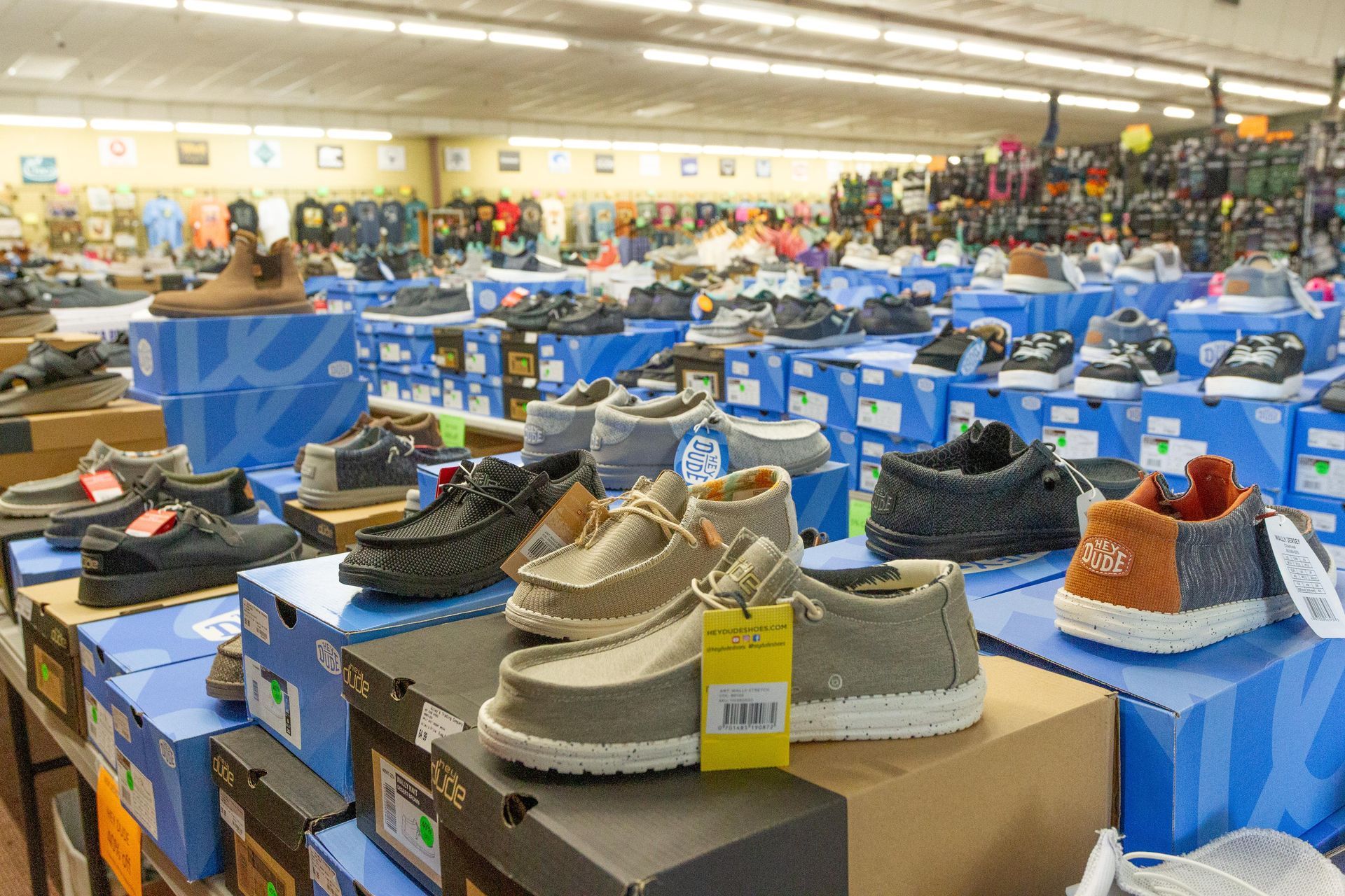 Shoes on display in a store, arranged on blue and brown boxes. Various styles and colors are visible, with more merchandise in the background.