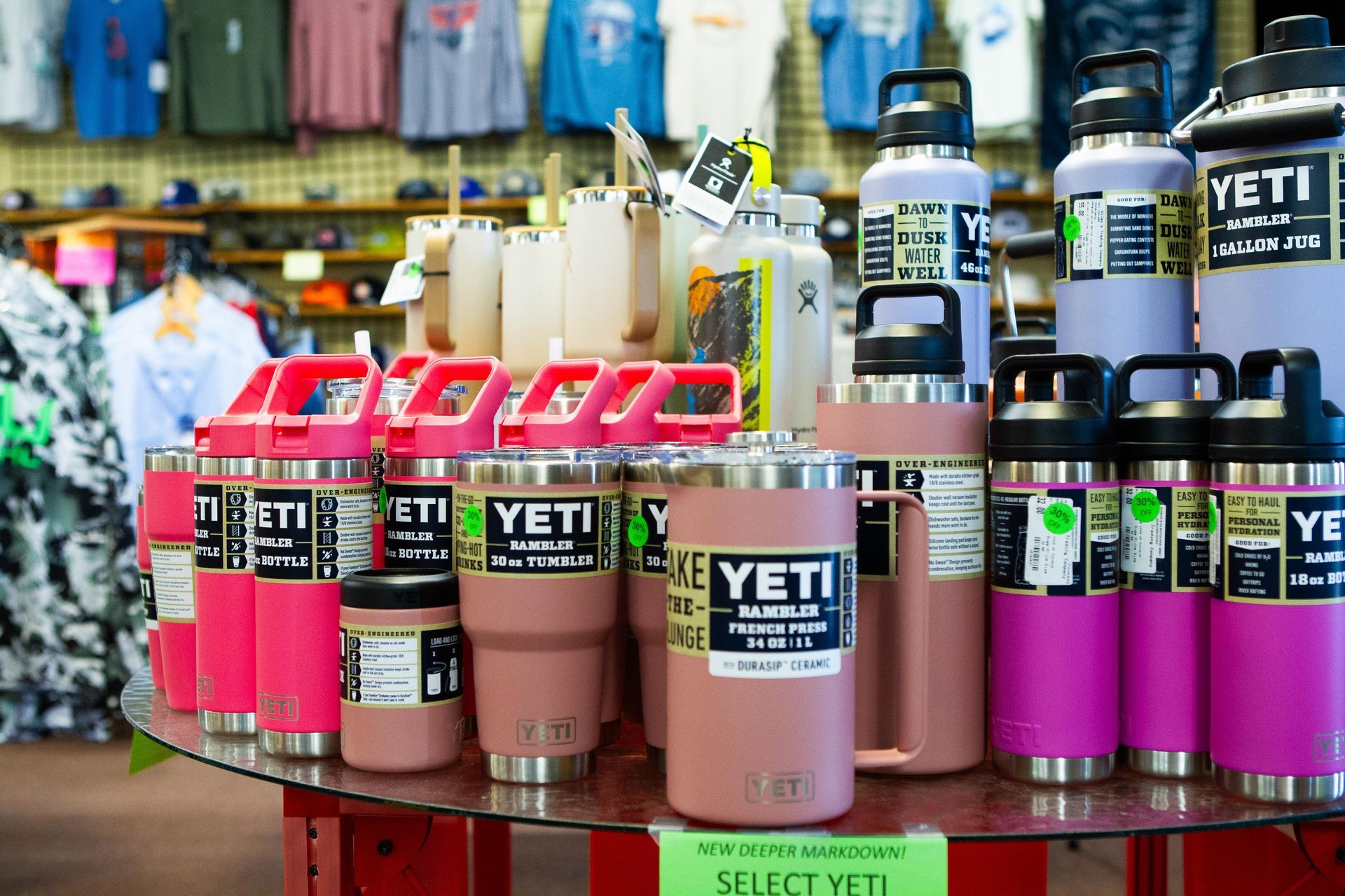 Display of pink and stainless steel Yeti drinkware on a circular table in a store. T-shirts are visible in the background.