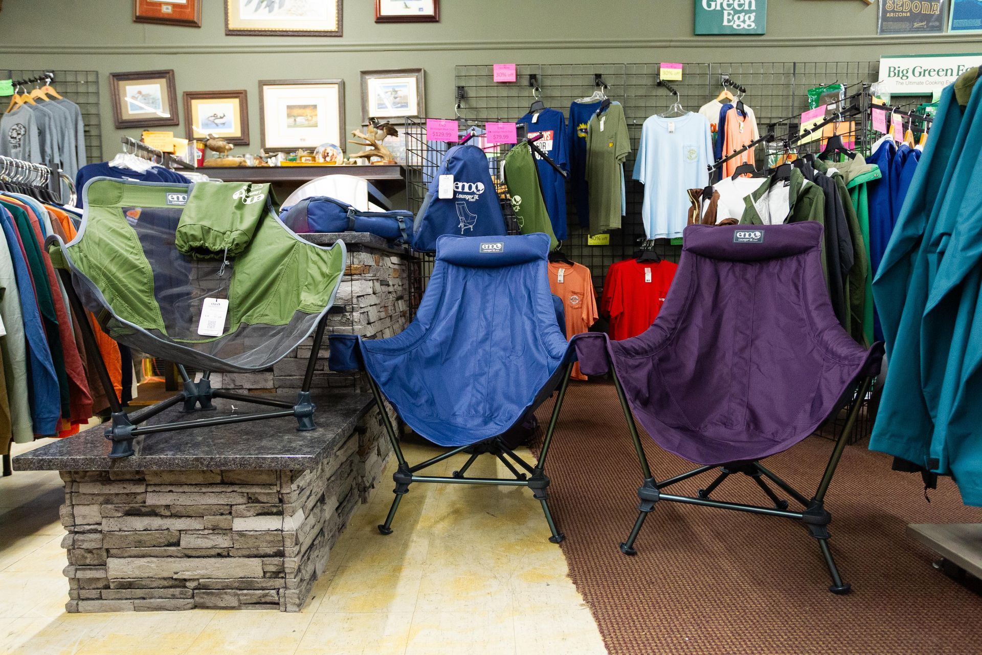Indoor shot of a retail store displaying outdoor camping chairs in blue and purple, with clothing racks in the background.