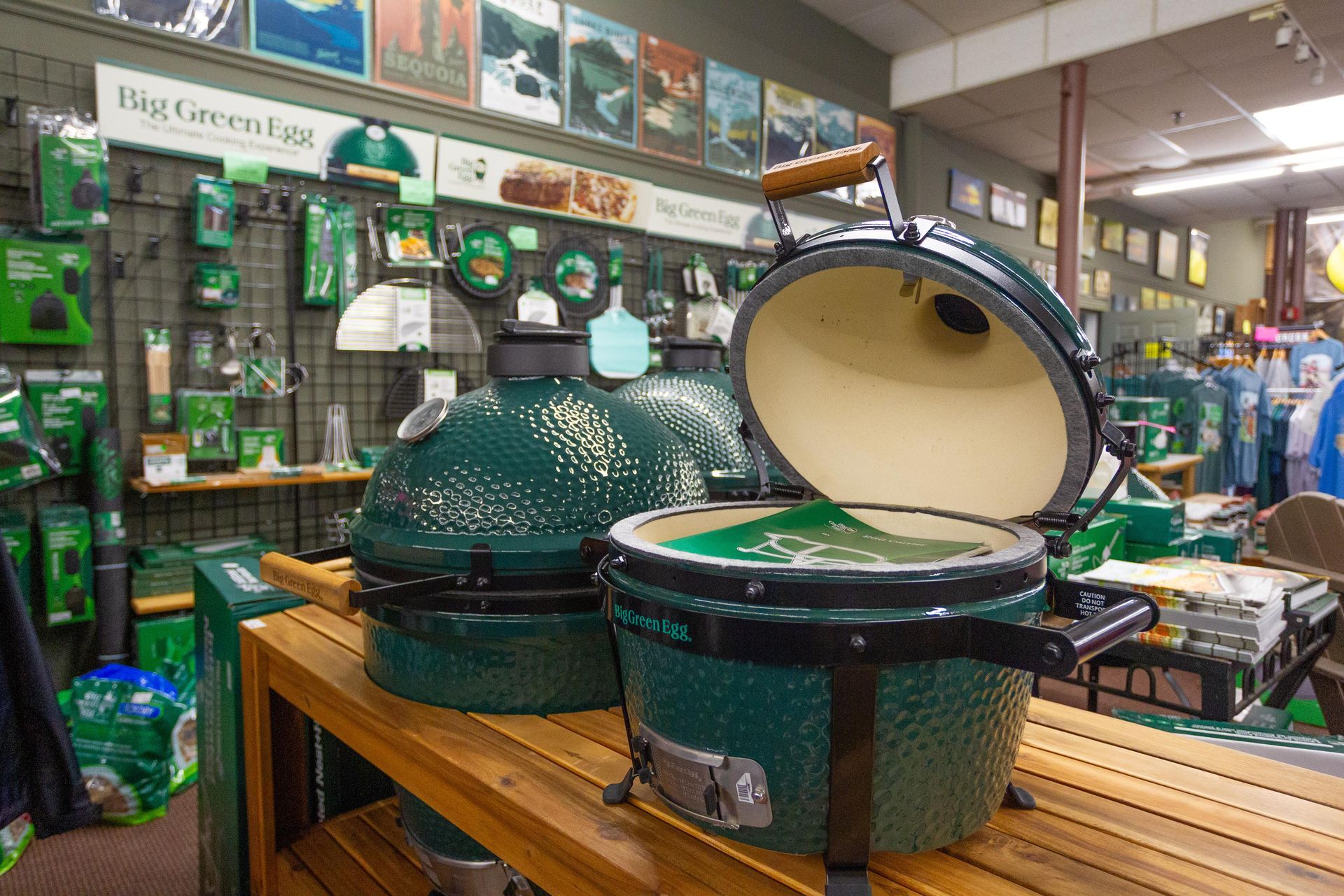 Green Big Green Egg grills on display in a store with accessories and Big Green Egg signage.