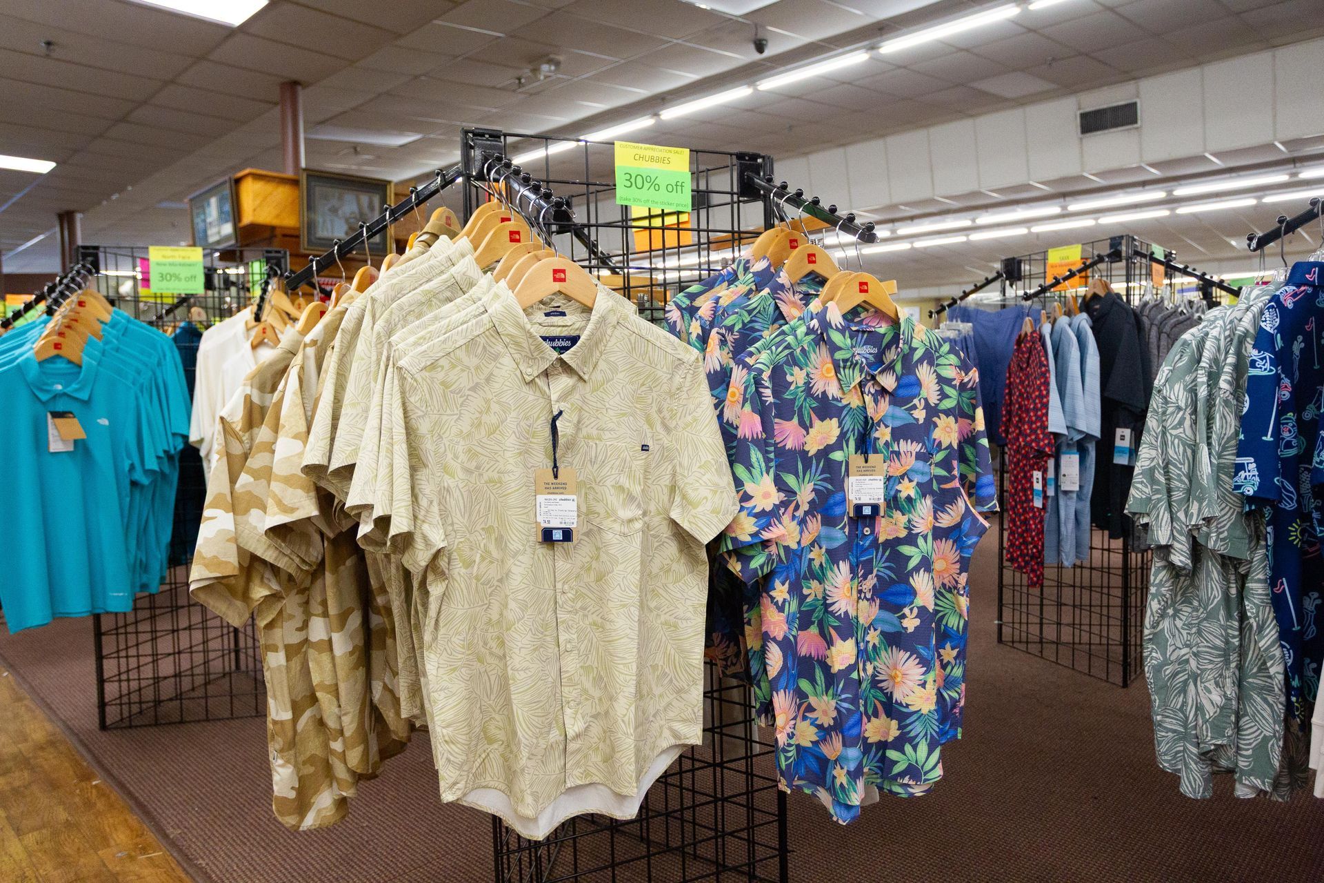 Men's shirts on display in a clothing store. Various patterned short-sleeved button-downs hang on racks.